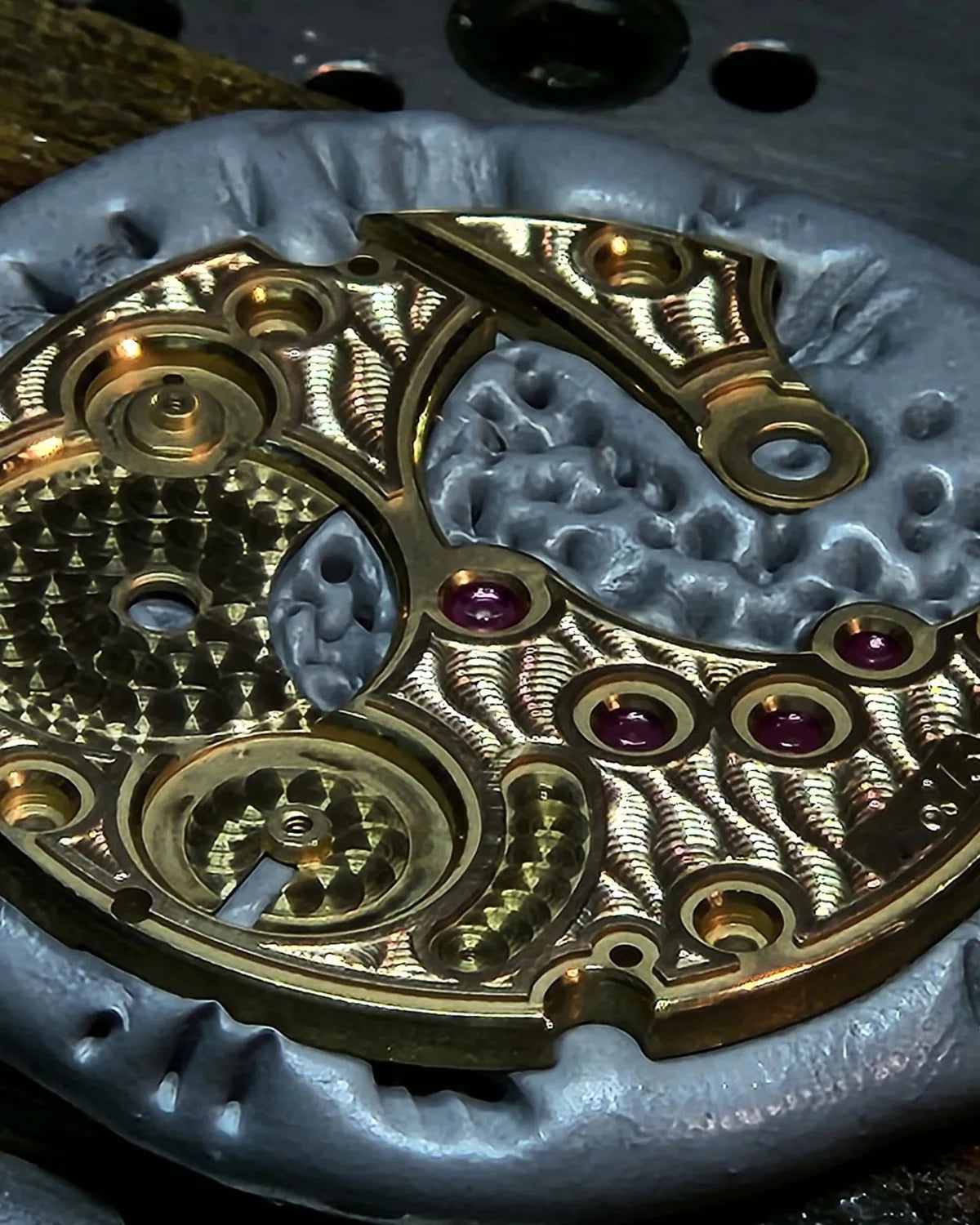 A gold mainplate held in the watchmaker's putty, circular-grained and set with ruby jewels